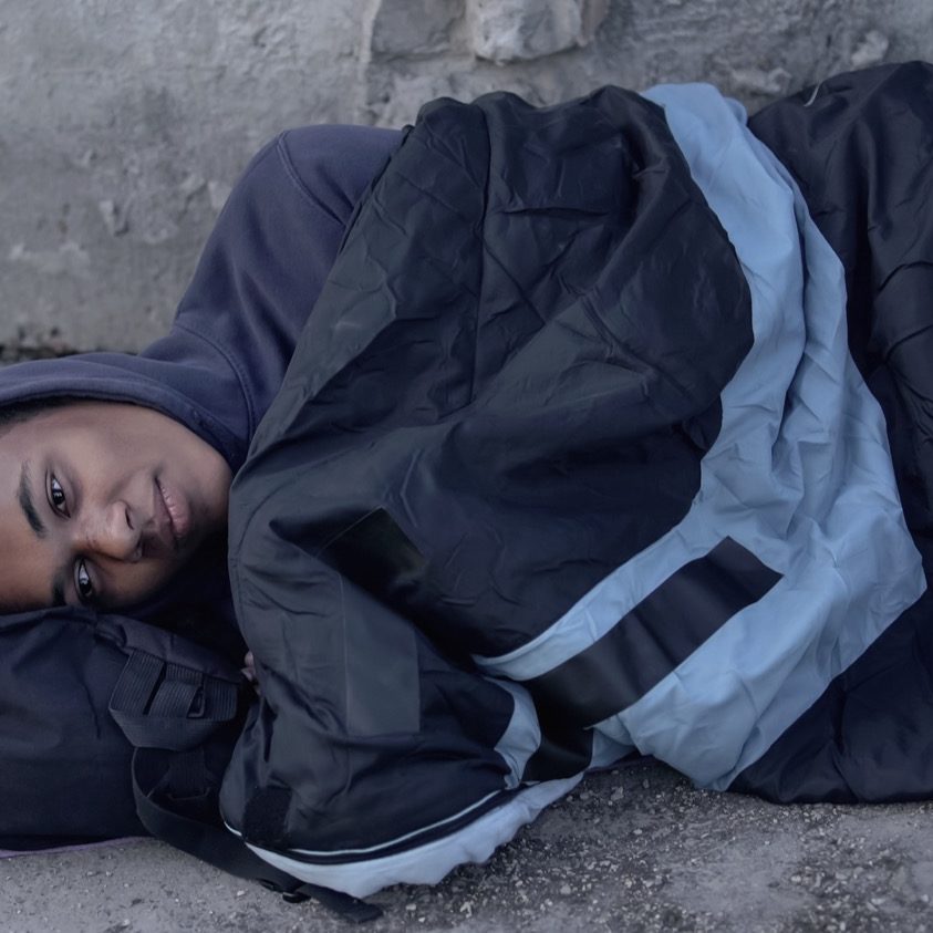 Desperate black man lying street covered with sleeping bag, poverty hopelessness